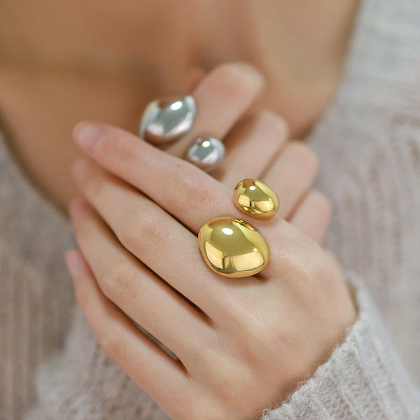 Uma mão mostrando 2 anéis geométricos JZ1547 em dourado e prateado